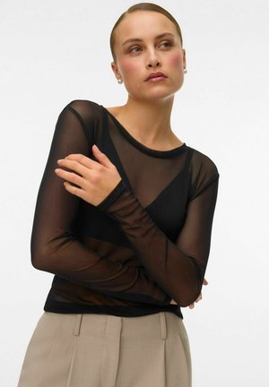 Zwarte langemouwen top gemaakt van doorzichtig materiaal, met een ronde hals en aansluitende mouwen, gedragen met beige high-waisted broek.