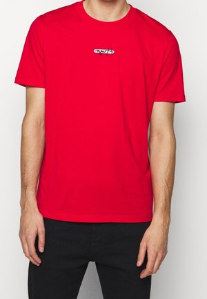 Rød bomulds t-shirt med korte ærmer, rund hals, med et lille, stiliseret logo i hvid og sort centreret på brystet.