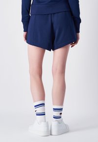 Shorts sportivi di colore blu navy con una vestibilità ampia, caratterizzati da una vita con coulisse e un orlo curvato. Abbinati a calze bianche con strisce blu.