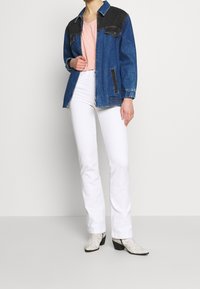 Giubbotto di jeans con dettagli neri sulle spalle sopra una camicia rosa chiaro, abbinato a pantaloni bianchi flair e stivaletti alla caviglia con stampa rettile testurizzata.