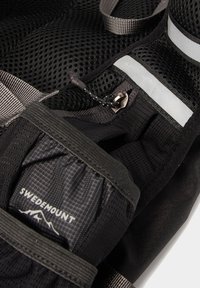 Schwarze Netztragetasche mit verstellbaren Trägern, reflektierenden Akzenten und einer Reißverschlusstasche mit dem "Swedemount"-Logo. Texturierte Materialien bieten Grip.