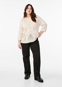 Pull en maille beige à coupe loose et manches trois-quarts, associé à un pantalon noir ajusté et des chaussures à plateforme noires.