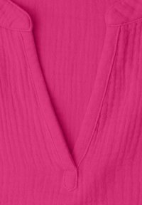 Gros plan d’un tissu texturé rose vif avec un décolleté en V et un petit bouton recouvert de tissu en bas au centre.
