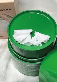 Zielony balsam do oczyszczania w okrągłym pojemniku, z białym, teksturowanym produktem wewnątrz, w gładkim i błyszczącym zielonym opakowaniu.