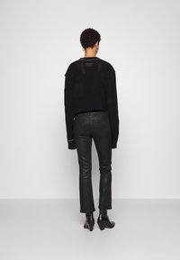 Jersey negro de punto con mangas largas y un patrón texturizado, combinado con pantalones de cuero negro ajustados y botines negros de tacón.