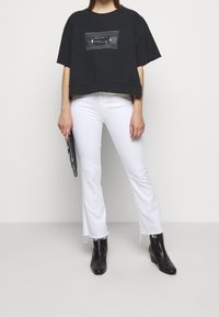 Mustat lyhyet t-paidat, joissa on vintage-kassettigrafiikka, yhdistetty valkoisiin leveälahkeisiin farkkuihin. Mustat nilkkurit, joissa on pieni korko.