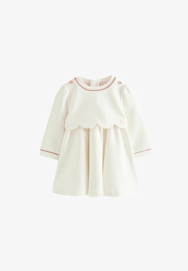 Šaty krémové barvy s dlouhými rukávy, zdobeným živůtkem s vlnkovaným okrajem, růžovým lemováním a dekorativními knoflíky na ramenech; měkká látka, rozšířená sukně.