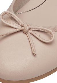 Gros plan sur une ballerine rose clair avec un nœud cousu sur l'avant arrondi et une semelle marron clair.