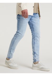 Ljusblå denimjeans med smal passform, lätt blekning och minimal whiskering. Matchas med vita sneakers och en neutral-tonad topp.