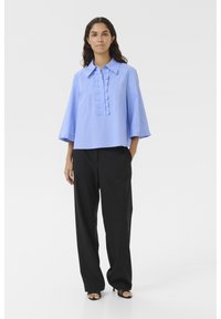 Light blue striped shirt with a folded collar, front pleats, and three-quarter sleeves, paired with black wide-leg pants and open-toe sandals.