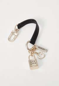 Nyckelring med ett svart läderband, gyllene detaljer, en låsberlock med ingraverad "EST 1981", och taggar som visar "GUESS" och "G"-detaljer.
