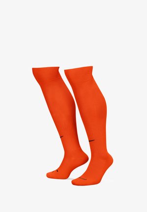 Kniestrümpfe in leuchtendem Orange mit geripptem Muster und glatter Oberfläche. Das schwarze Logo an der Sohle sorgt für einen Kontrast.