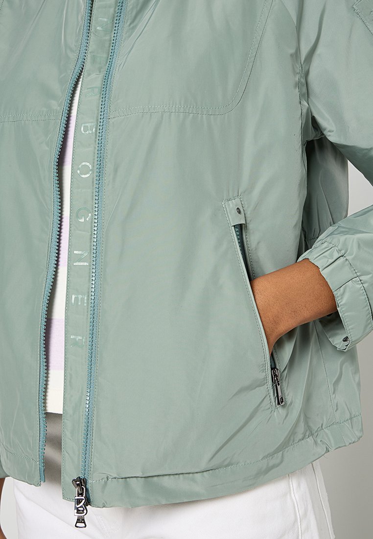 Hellegrüne, leichte Jacke mit Reißverschluss, seitlichen Taschen und elastischen Bündchen. Glatte Textur und minimalistisches Design.