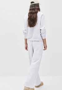 Hellgrauer Sweatshirt und passende weit geschnittene Hose aus weichem Baumwollgemisch, mit gerippten Bündchen und lockerer Passform, kombiniert mit beigen Schuhen.