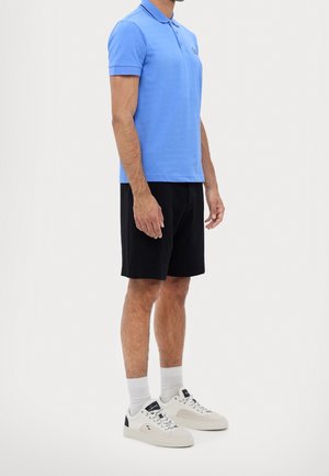 Jasnoniebieska koszulka polo z krótkim rękawem, czarne spodenki i białe tenisówki. Polo ma kołnierzyk i subtelne logo na piersi.