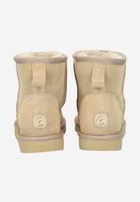 Botas de tobillo de ante color tostado con un suave forro interior, suelas planas y un pequeño parche con el logo en la parte posterior. Presenta costuras reforzadas y tiradores.