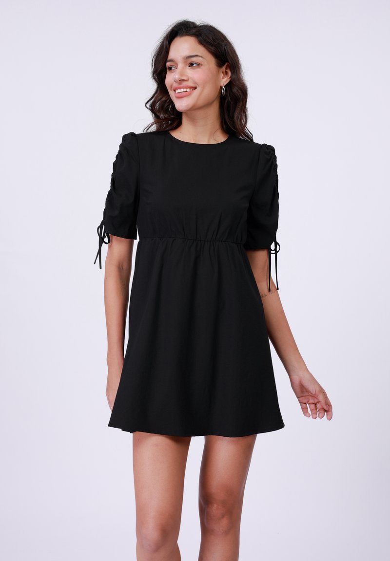 Vestido negro corto hecho de tela suave. Presenta mangas abullonadas con detalles de cordón y un corte relajado que se ensancha en el dobladillo.