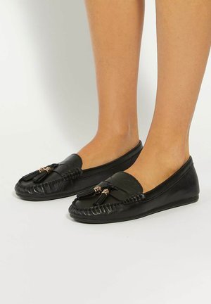 Black leather loafers featuring a smooth finish, front tassel accents, and a flexible sole. Rounded toe with stitched detailing.