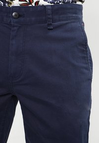 Kalhoty z bavlněného směsového materiálu v námořnické modré barvě s jemnou texturou, vybavené přední kapsou, zapínáním na jeden knoflík a prošitím na švech.
