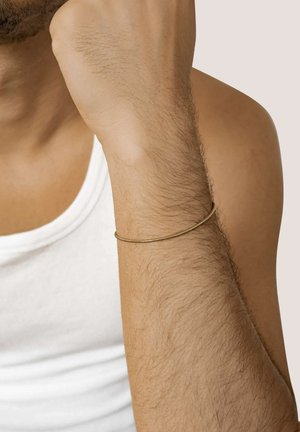 Goldenes Armband an einem Handgelenk, das ein glattes, rundes Design aufweist. Der Hautton steht im Kontrast zum metallischen Glanz des Armbands.