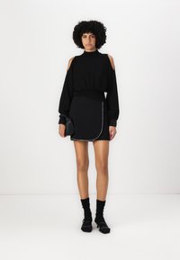 Black high-neck sweater with shoulder cutouts, paired with a black mini skirt featuring a side slant and contrasting trim, worn with black socks.
