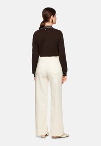 Schwarzer Langarmpullover mit gestreiftem Kragen, kombiniert mit hoch taillierten, weiten weißen Jeans. Glatter Stoff und minimalistisches Design.