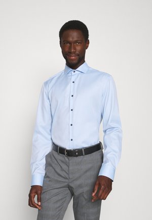 Lichtblauw overhemd met lange mouwen en een button-down kraag, zwarte knopen en een gladde stof. Gecombineerd met grijs geruite broek en een zwarte riem.