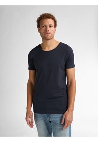 Tricou cu mânecă scurtă de culoare albastru închis, dintr-un material moale, cu decolteu rotund, formă ajustată și textură netedă, asortat cu blugi de culoare albastru deschis.