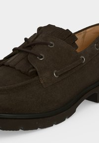 Mocassin en daim brun foncé avec détail à franges, œillets pour lacets et semelle noire épaisse avec crampons, vu de profil.