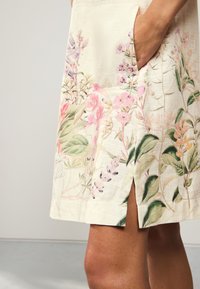Robe à imprimé floral en tissu léger, présentant des motifs botaniques roses et verts, avec des poches latérales et une fente au niveau de l'ourlet.