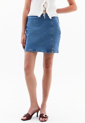 Blå denim miniskørt med en tætsiddende design, rå kant og lynlås i siden. Kombineret med brune hæl-mules med et guldaccent.