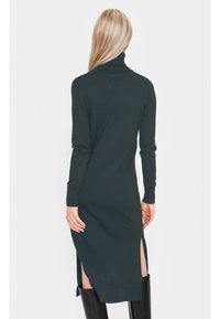 Tummanvihreä ribbikuvioinen neulemekko, jossa on korkea kaulus, pitkät hihat ja sivuhalkiot liikkuvuuden lisäämiseksi. Ei näkyviä kuvioita tai koristeita.