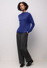 Gestrickter blauer Pullover mit hohem Kragen, weiter Passform; kombiniert mit grauen, weit geschnittenen Hosen und schwarzen Schuhen. Glatte Textur und lässiges Design.