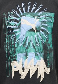 Λογότυπο Puma με πηδώντας γάτα σε κρεμ χρώμα, περιβαλλόμενο από υφασματικό μπλε και πράσινο αφηρημένο σχέδιο και έντονο στιλιζαρισμένο κείμενο "PUMA" σε μαύρο φόντο.