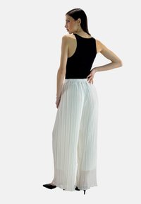Black sleeveless top paired with white pleated wide-leg pants, featuring an elastic waistband. The pants are semi-sheer with a flowing texture.