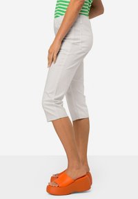 Lichtgrijze cropped broek met een gladde textuur, voorzien van achterzakken en een recht model, gecombineerd met fel oranje platform sandalen.