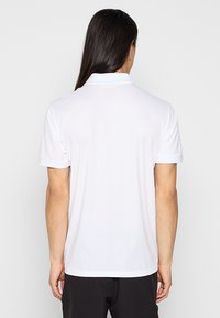 Camisa polo blanca de manga corta, con cuello y una textura suave. Las características incluyen un color sólido sin patrones ni marcas visibles.