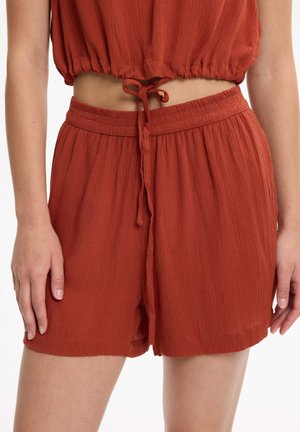 Pantalones cortos de tela texturizada color óxido con cintura elástica y cordón, usados con un top corto a juego que deja al descubierto el abdomen.