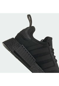 Černá sportovní bota s texturovaným svrškem, designem se třemi pruhy, gumovou podrážkou a poutkem na patě pro snadné obouvání.