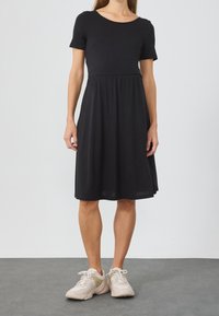 Černé krátké šaty s kulatým výstřihem, přiléhavým živůtkem a rozšířenou sukní. Nošeno s světle zbarvenými teniskami.