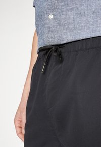 Schwarze Shorts mit Kordelzug aus leichtem Stoff, mit einer glatten Textur und Seiten Taschen, kombiniert mit einem strukturierten, blauem Hemd mit Knöpfen.