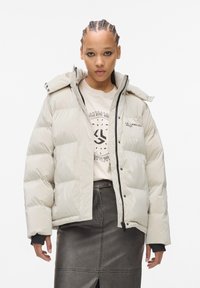 Dikke witte jas met een hoge kraag, rits aan de voorkant en drukknoopjes. Gekleed over een beige graphic t-shirt en een zwarte leren rok.