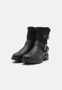 Bottines noires avec un nez en cuir lisse, une doublure en fausse fourrure noire douce et des sangles réglables avec des boucles en métal. Semelle plate en caoutchouc.