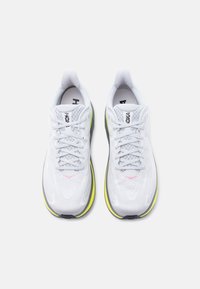 Ζευγάρι λευκών αθλητικών παπουτσιών με ανοιχτό γκρι κορδόνια, επάνω μέρος από δίχτυ, ενδιάμεσα σόλες σε νεον κίτρινο και μαύρες εξωτερικές σόλες, ορατά από πάνω σε λευκό φόντο.