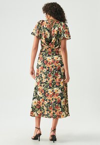 Gėlėta midi suknelė su trumpomis prisiūtomis rankovėmis, juodu fonu, ryškiomis oranžinėmis ir geltonomis gėlėmis, surišta nugaroje ir laisvai krintanti.