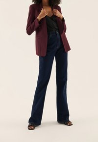 Burgunderfärgad kavaj över en svart satinblus, kombinerat med högmidjade mörkblå utsvängda jeans och svarta klacksandaler. Enkla accessoarer ingick.