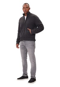 Dunkelgrauer, gestrickter Reißverschluss-Pullover mit gerippten Säumen, kombiniert mit hellgrauen Jeans und schwarzen Sneakern. Gemütliche Textur und figurbetontes Design.