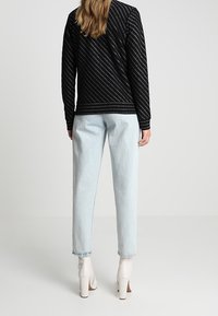 Zwarte gebreide trui met diagonale strepen, gecombineerd met lichtblauwe high-waisted jeans en witte enkelbooties.