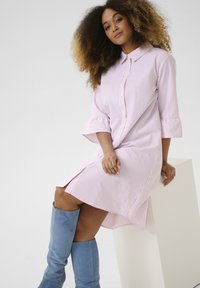 Abito camicia a righe in rosa chiaro e bianco, con apertura a bottoni sul fronte, colletto e maniche a tre quarti, abbinato a stivali blu al ginocchio.
