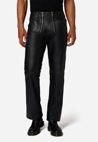 Zwarte leren broek met een rechte snit, twee stevige voorzakken met rits en een gladde textuur, gecombineerd met zwarte laarzen.